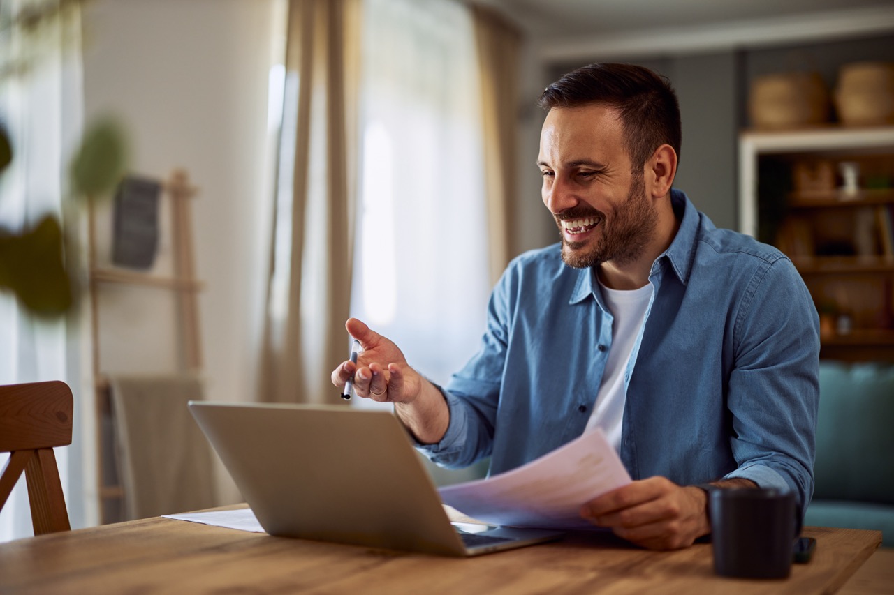 A happy adult hiring manager laughing with a candidate in an online interview while holding his resume papers. Person in Minneapolis in an interview holding their resume