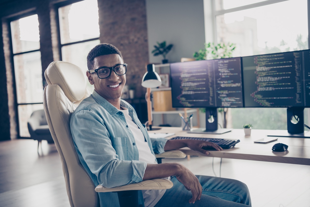 Portrait of young smiling guy sitting armchair smart senior devops professional programmer control cyber security at work place in office